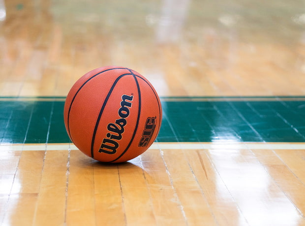 image of a A Wilson basketball sitting on a polished wooden court with a green out-of-bounds line
