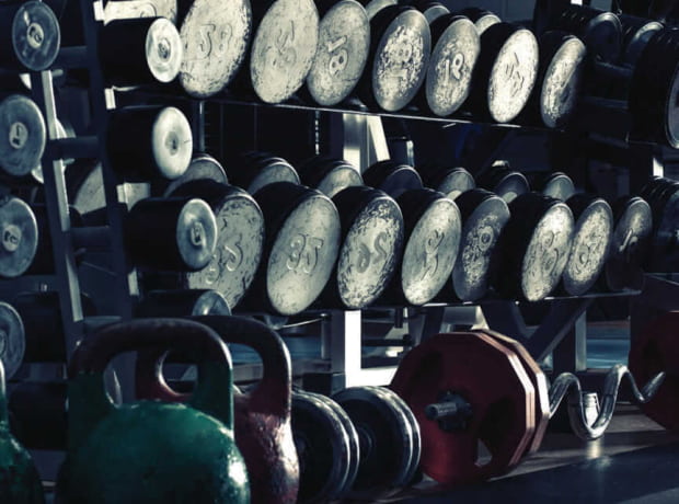 image of a gym weight rack holding various dumbbells labeled with weights like 35 and 18 pounds, with kettlebells and additional weights in the foreground