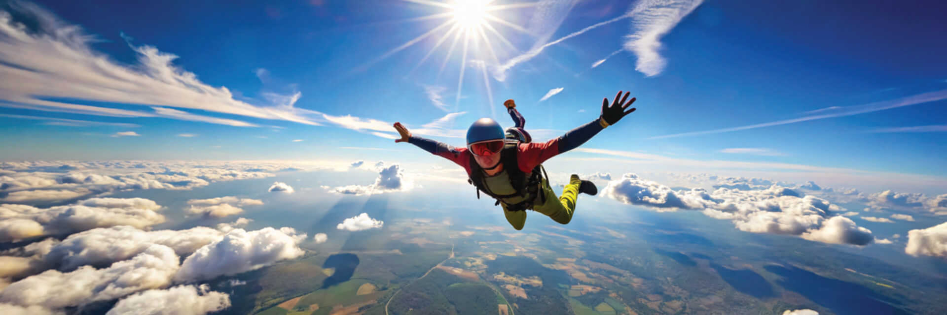 image of a skydiver in a helmet and colorful jumpsuit soaring through the sky with arms and legs spread, above a landscape of fields and forests, under a bright sun with scattered clouds