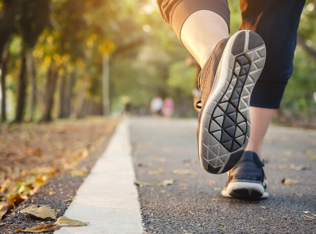 a close-up image of a person jogging on a paved path in a park